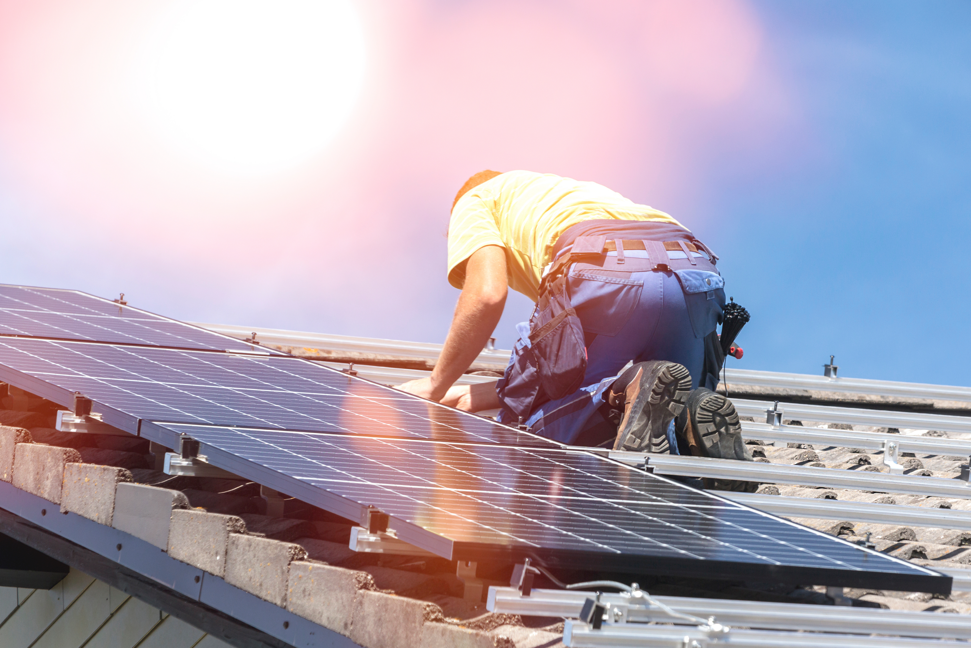 Monteur der auf einem Dach PV-Module anbringt.