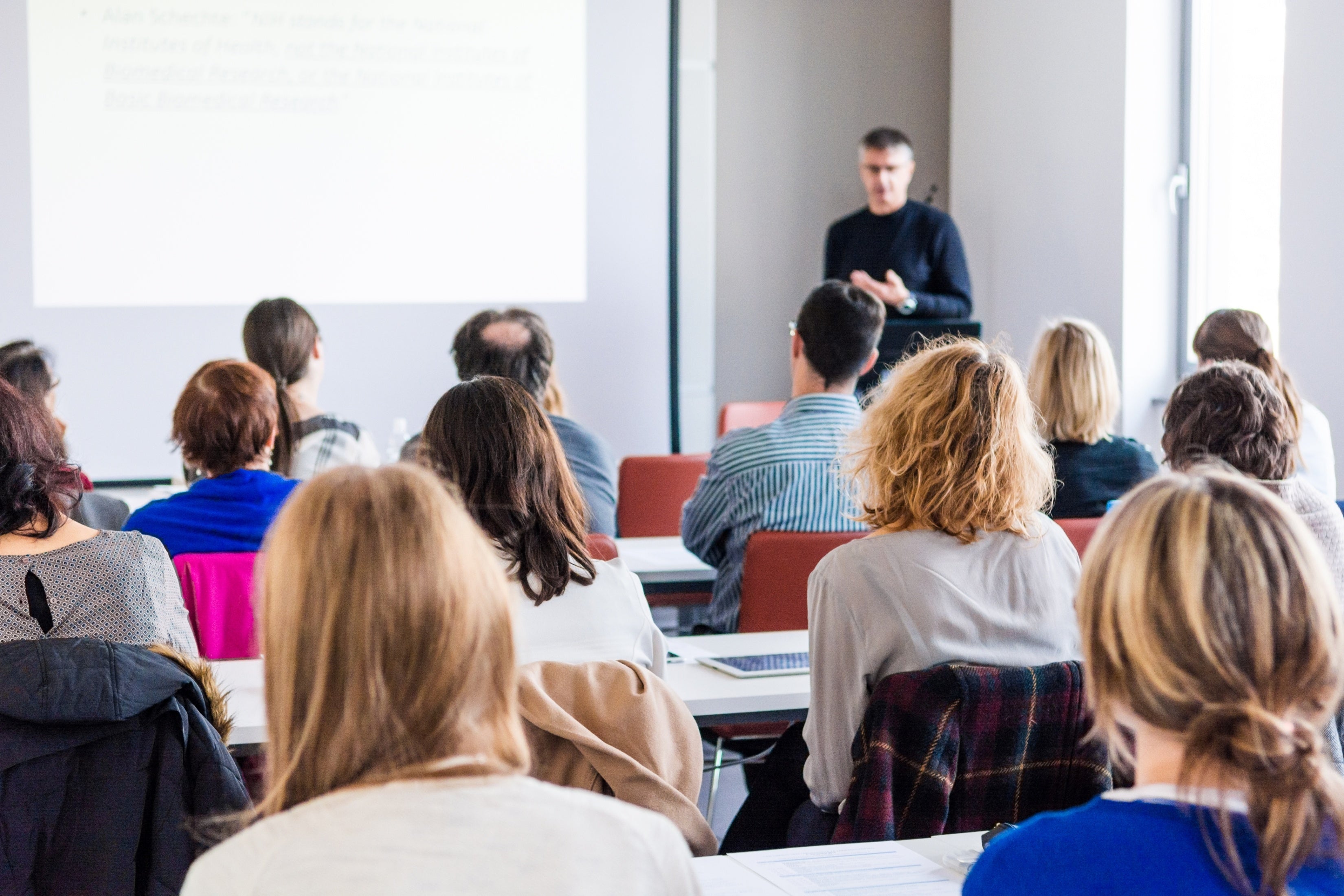 Schulungsveranstaltung mit Referent und Publikum in einem Seminarraum.